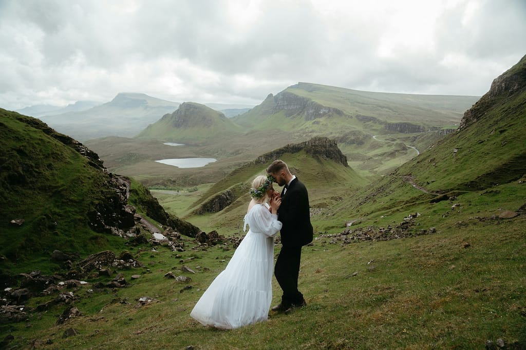 A bride and groom standing on a grassy hill in the mists of Scotland