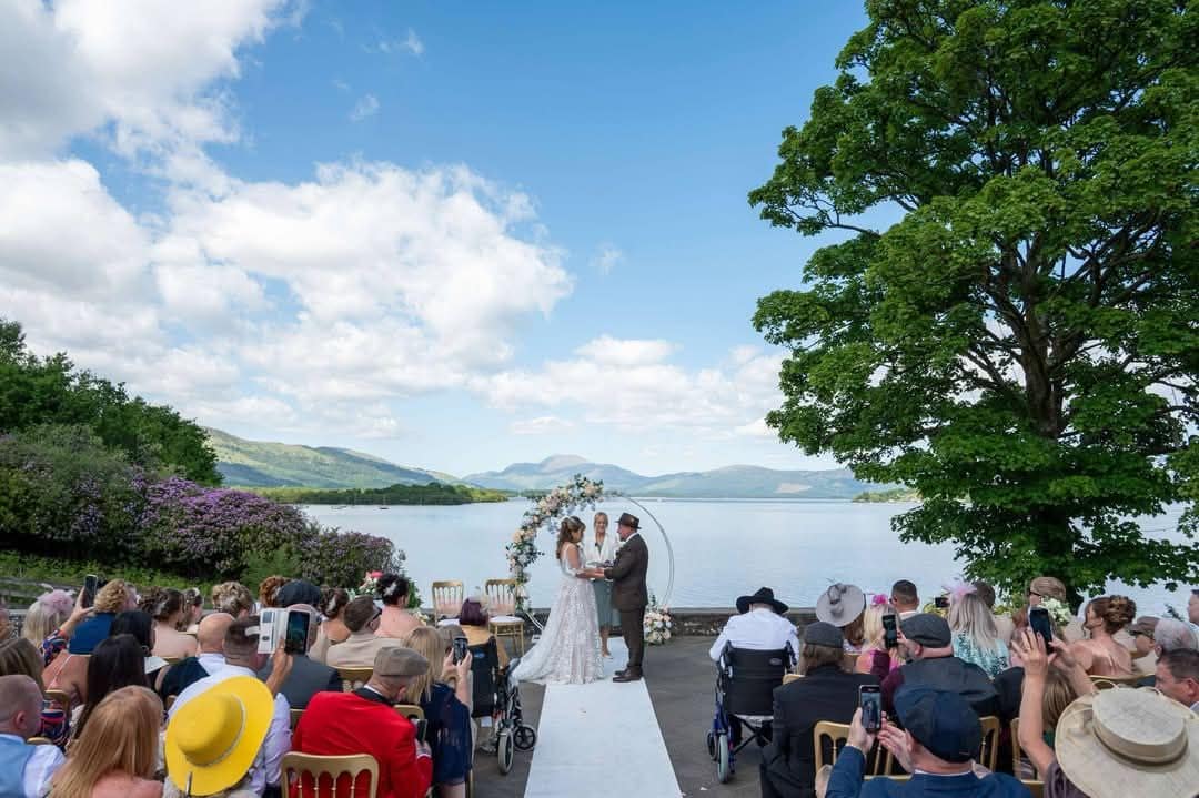 Couple holding hands in front of assembled wedding guests at Loch Lomond with Fleur as the celebrant