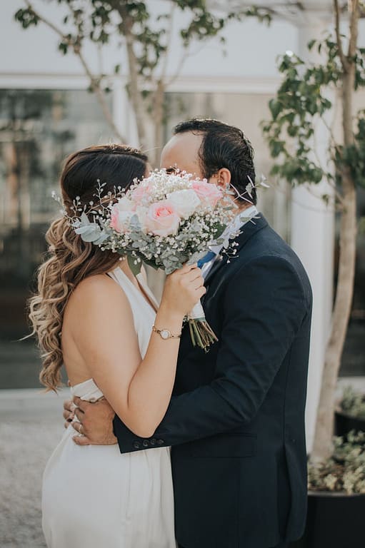 Bride and groom share a tender embrace outdoors, hidden by a beautiful bouquet.