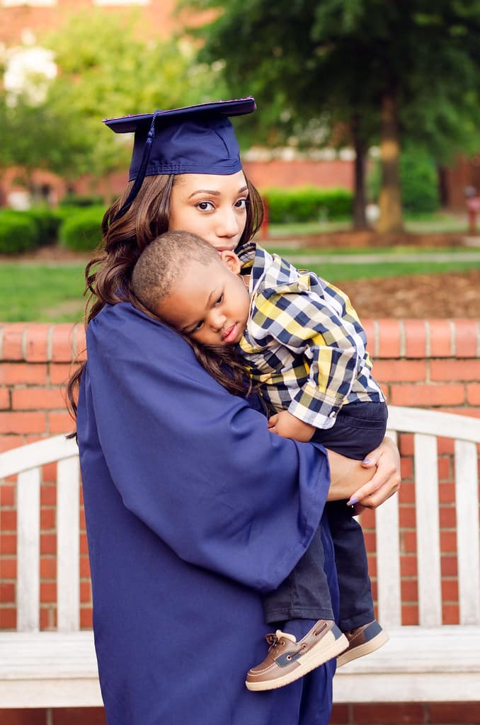 Woman in graduation gown, holding toddler.