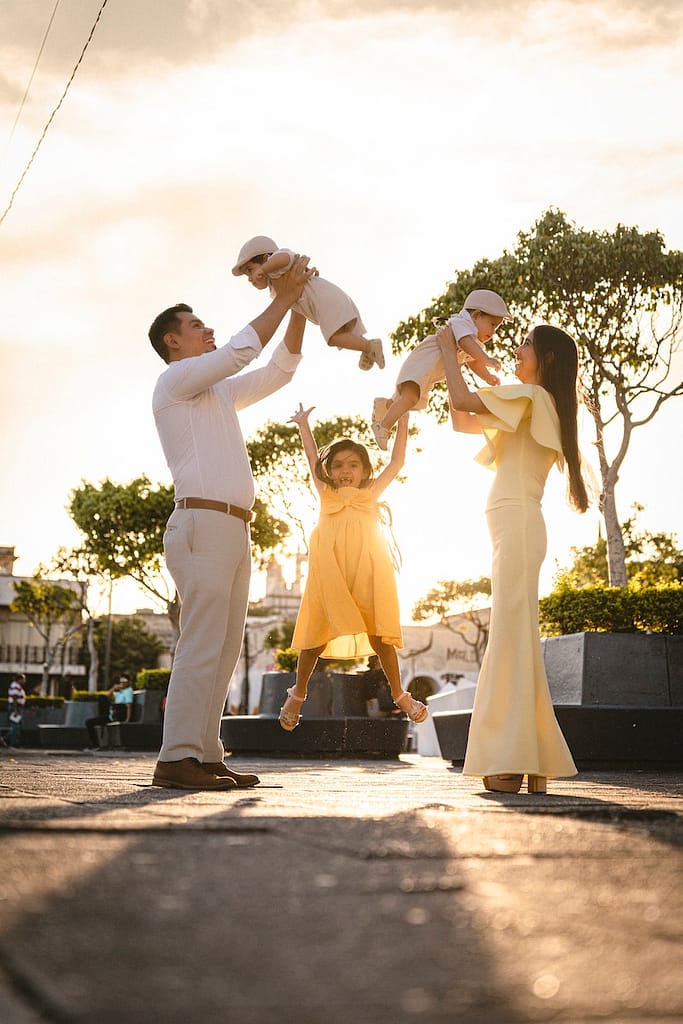 Two parents joyfully hoist their baby and little girl into the air