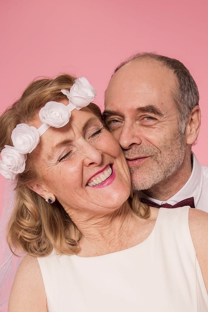 Happy elderly couple embracing with smiles against a pink studio background.