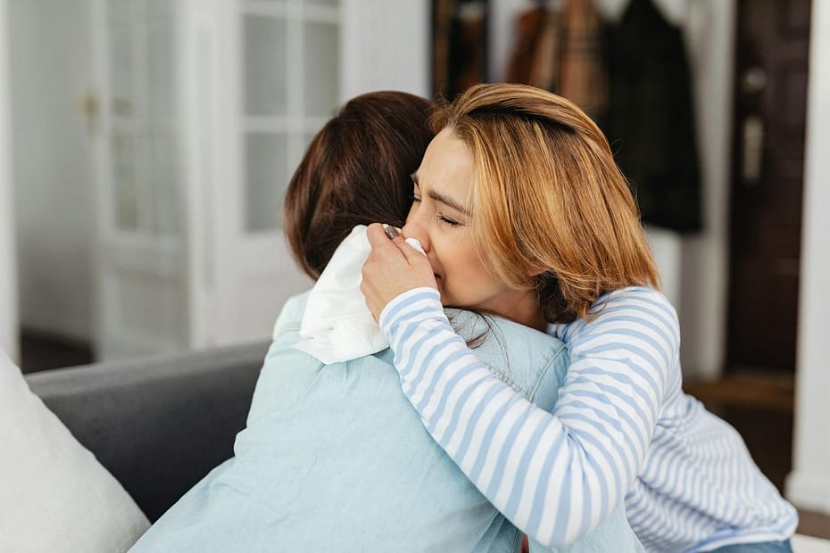 Two women sharing an emotional embrace indoors, offering comfort and support.