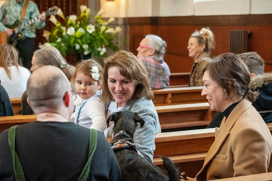 a group of people, including a child sitting in pews with a dog